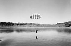 Person with parachute nears water landing area in lake.