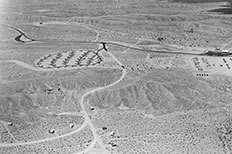 Aerial view of horizontally paved road running through the desert landscape with dirt roads stemming in all directions, camping area in upper left.