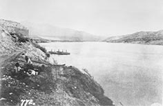 Two people sit near cliff overlooking a lake.