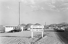 Small building to the left with road on right, sign in center points to Swimming and Public Campgrounds.