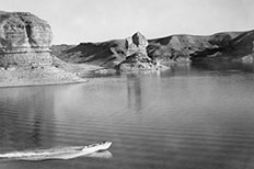 Speed boat traveling through a large body of water surrounded by towering rock formations and mountains.