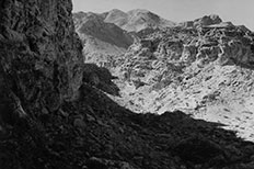 Textured mountain in shadows to the left , sunlit valley and rugged hill to right.