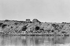 Two parallel rectangular-shaped brick ruins on top of desert landscape with a body of water below. 