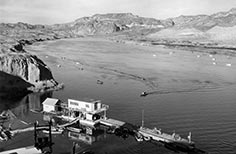 Two level boat dock lower left on river with many boats, rolling desert hills and mountains in distance.