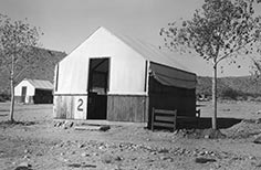 Cabin with a tent roof, wood bed frame outside to right.