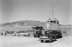 Two trucks next to boat on boat trailer nearby a lake with a dock on it.