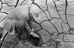 Man kneels near hole in dried up and cracked dirt.
