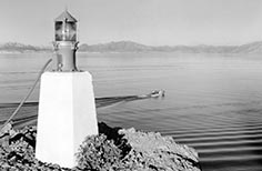 Light beacon at edge of cliff overlooking lake with a boat on it.