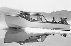 Boat with reflection in water, six people at back of the boat.