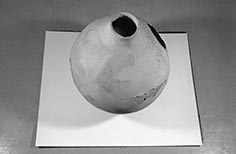 Pottery vessel with narrow opening broken hole at right and flaking material lower right.