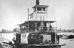 Paddlewheel boat named Searchlight with many people on lower and upper deck.