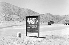 Lake Mead construction sign in desert with trucks in background.