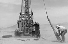Two men in a dust storm operating an earth drilling rig .