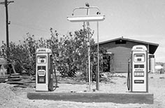 Two gas pumps with building and foliage behind them.