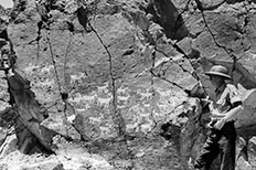 Ranger stands next to a cracked mountain that has ram-like petrolglyps scattered across it.