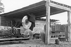 Saw carriage and headsaw with a wooden shelter-like formation surrounding it. 

