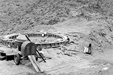 A ring-shaped water tank foundation in desert, cement mixer in foreground. 