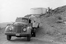 Circular-shaped tank sits on top of a dirt hill with a parked pick-up truck at the bottom.
