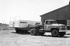 Large truck with trailer containing two swimming rafts, metal building in background.