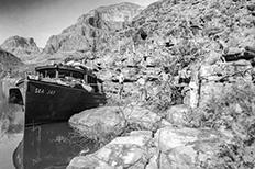 A boat sits in a body of water as a group of boys and men stand next to it within rock formations and plants.