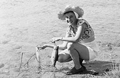 Woman squats down next to lake with two fish on a rope in her hands.