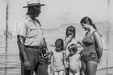 Uniformed Park Ranger and Lifeguard talking to young swimmers on the sand at the beach.