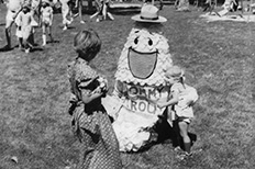 Tommy Trout puppet-like mascot sitting down in grass as he entertains small children. 