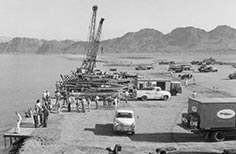 Many boats and small crowd of people near a lake.