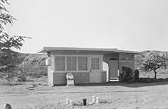 Front of small building with door, windows, and a trash can in that says Please.