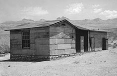 Small unfinished wood building with stone foundation in a desert.