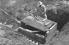 Man standing next to wood planks on small stone structure.