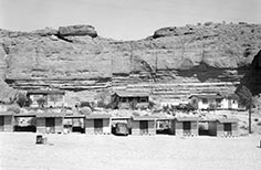 Small cabins and a few cars lined up in front of the side of a cliff range.