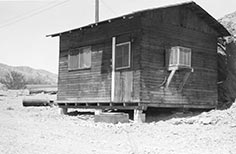 Front of a small wooden cabin with a cement slab used as a doorstep.