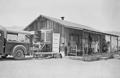 People stand on porch of wooden building with trucks parked nearby.