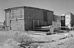 Small wooden building with bed frame out front.