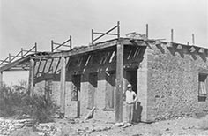 Man standing outside stone building with wooden columns.