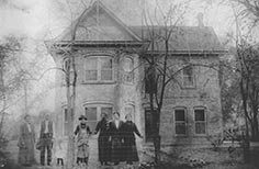 Group of people with two small children pose in front of brick house.
