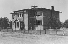Large brick building with wire fence around it and the words Public School on the front. 