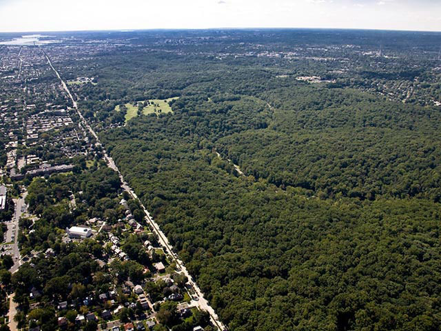 An aerial color photo showing the green forested area of Rock Creek Park surrounded by buildings, roads, parking lots, and developments. 