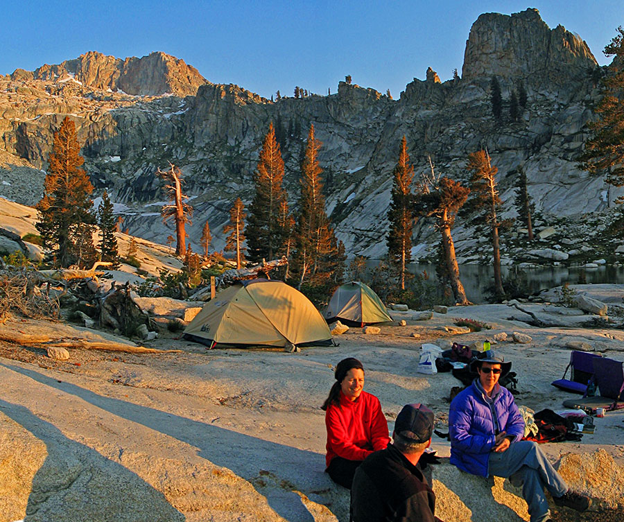 People sit near a tent among alpine peaks