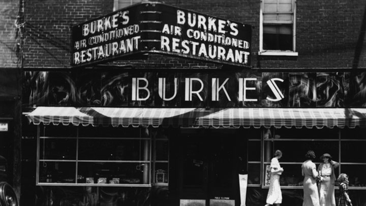 Restaurant storefront with three women and a young girl walking past.