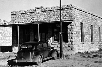 Brick bank with a 1930's era car parked outside the front entrance.