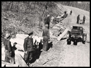 Eight men work at a roadside logging operation.