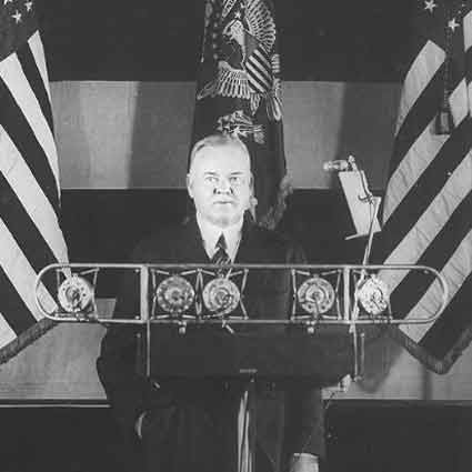 President Hoover speaking in front of microphones