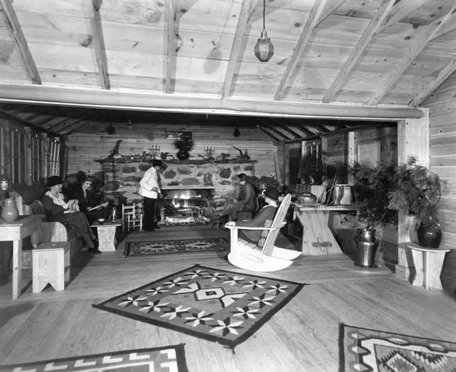 The living room containing four people in various seating in front of a fire stoked by a servant.