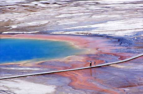 Two people standing on a boardwalk look out at Grand Prismatic Spring