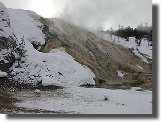 Water flows from a flat area and then down a steep ridge, creating a colorful hillside palette of brown, green, and orange.