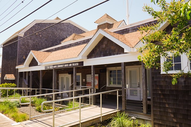 A cedar sided building with white trim. A sign above its main deck reads "Cherry Grove Community House and Theatre"