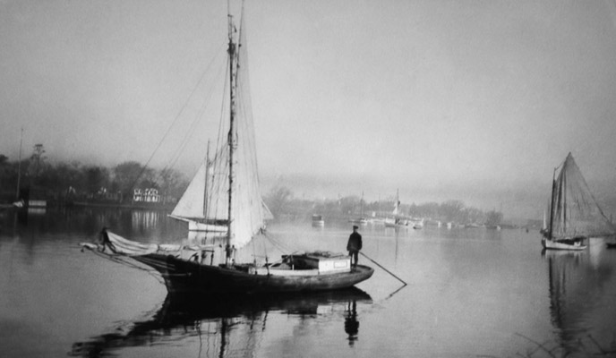 A black and white image of a Gil Smith boat floats on the Patchogue River. A black and white image of a Gil Smith boat floats on the Patchogue River.