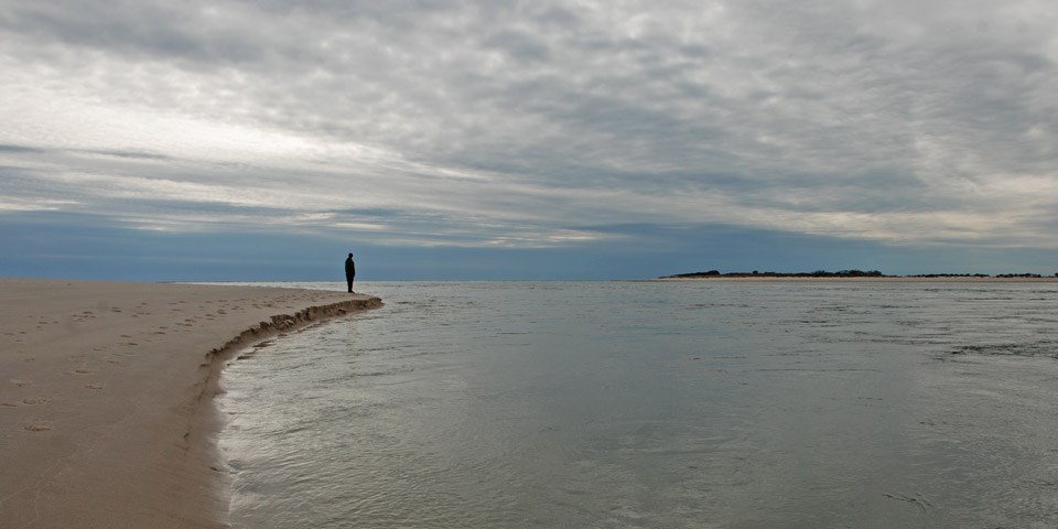 A person stands at the edge of the breach shoreline.